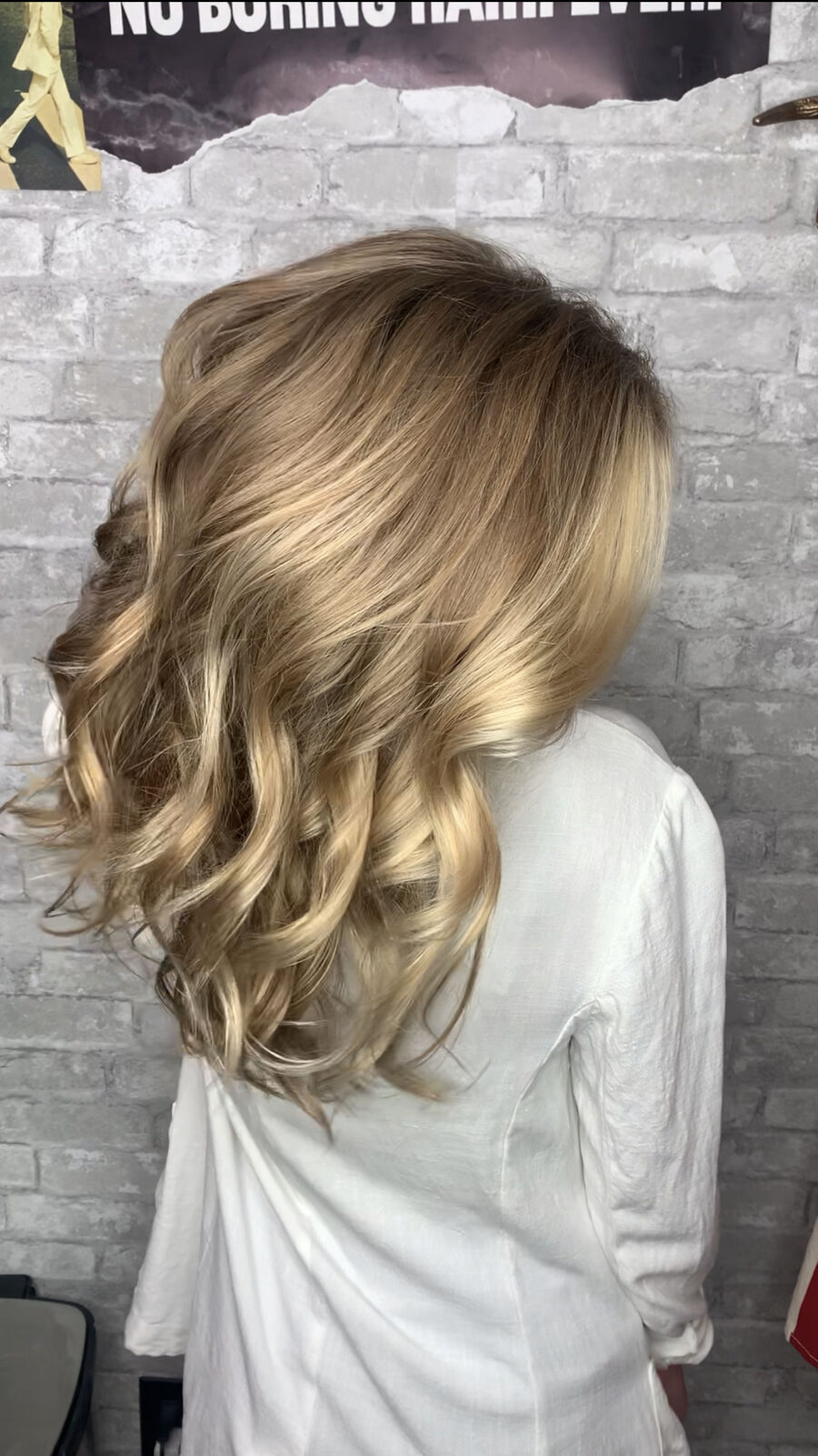 Wavy blonde balayage against brick wall